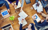 A group of people around a table comparing data.