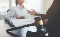 A lawyer and client discussing harassment in the workplace. Featured is a gavel and block, and uneven scales.