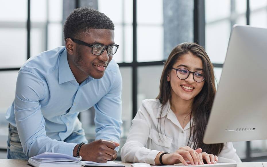 Two young professionals work together at a computer.