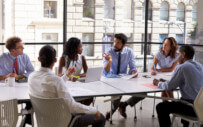 group of men and women sitting around a large table conversing